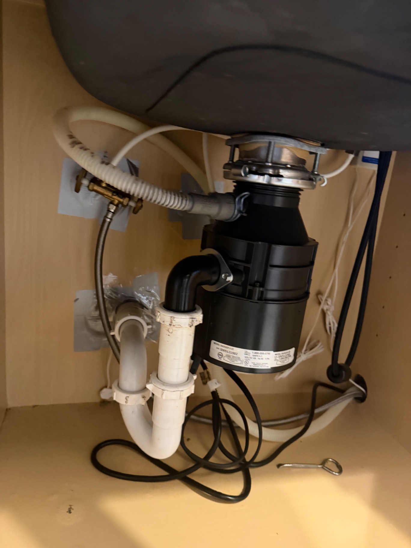 Newly installed InSinkErator Badger garbage disposal with dishwasher drain connection under a kitchen sink by BCS Plumbing