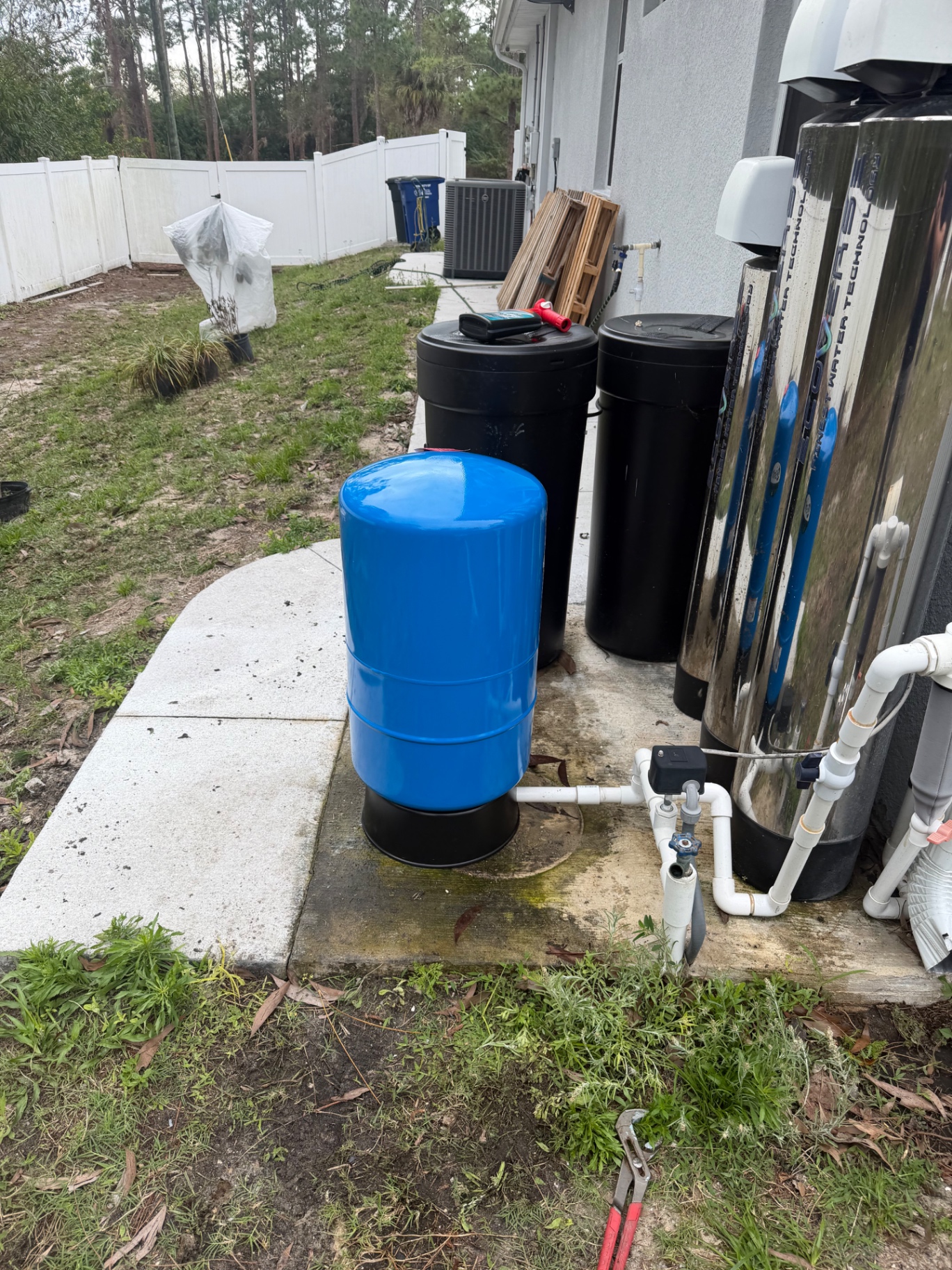 Blue bladder pressure tank and stainless softener/carbon filter tanks installed outside a Southwest Florida home by Better Call Sam Plumbing