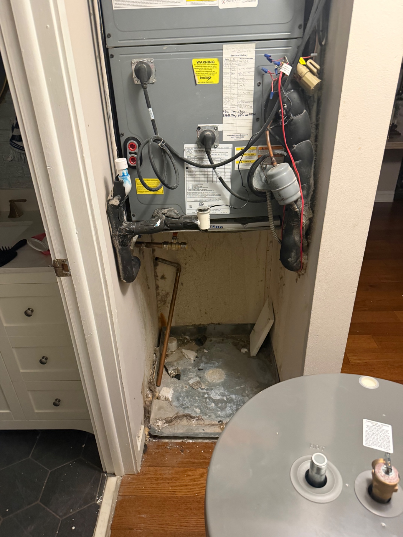 Leaking electric water heater removed from an interior closet next to an air handler by Better Call Sam Plumbing