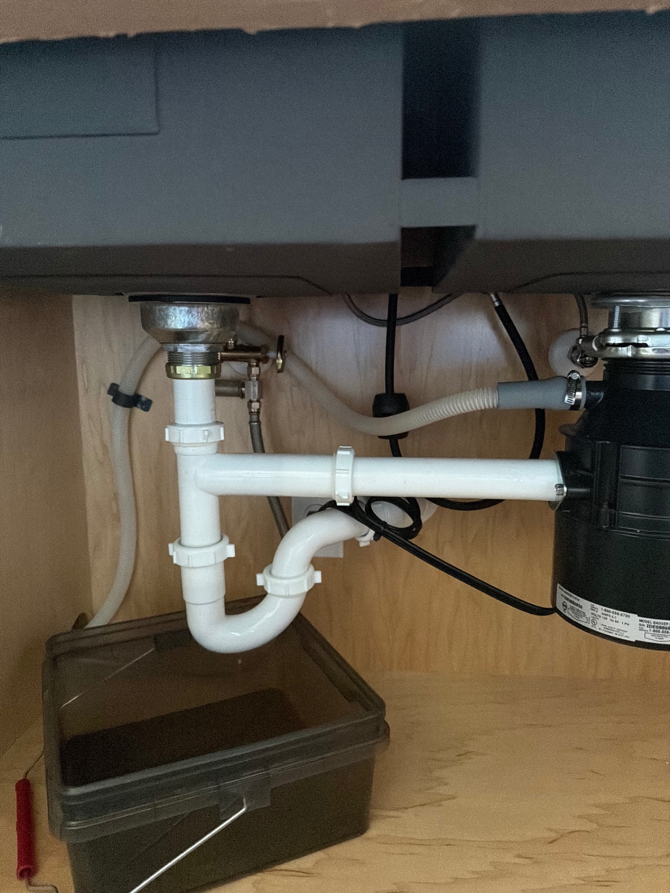 New PVC P-trap and drain assembly under a kitchen sink with garbage disposal and leak-detection tray installed by BCS Plumbing